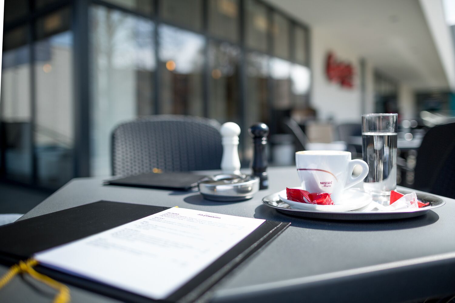 Un tavolo con un menu, una tazza di caffè, un bicchiere d'acqua e un piccolo contenitore per il sale.