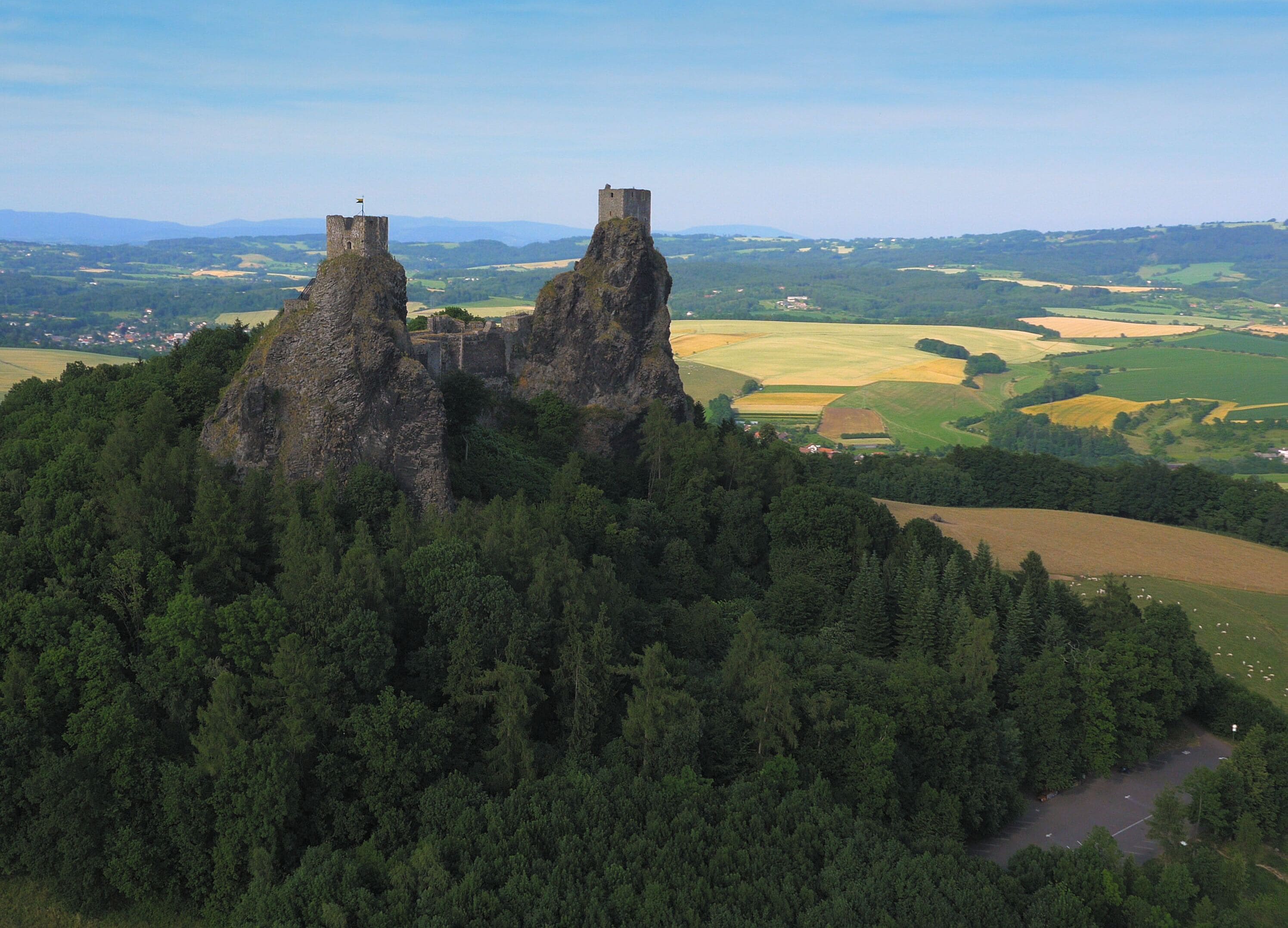 Un castillo en lo alto de una colina rocosa, con un primer plano arbolado y amplias vistas al campo.