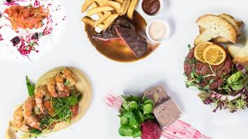 Une variété de plats, notamment des steaks, des frites et des crevettes, disposés sur une surface blanche.