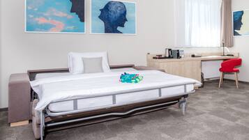 A hotel room with a bed, a desk, a chair, and artwork on the walls.