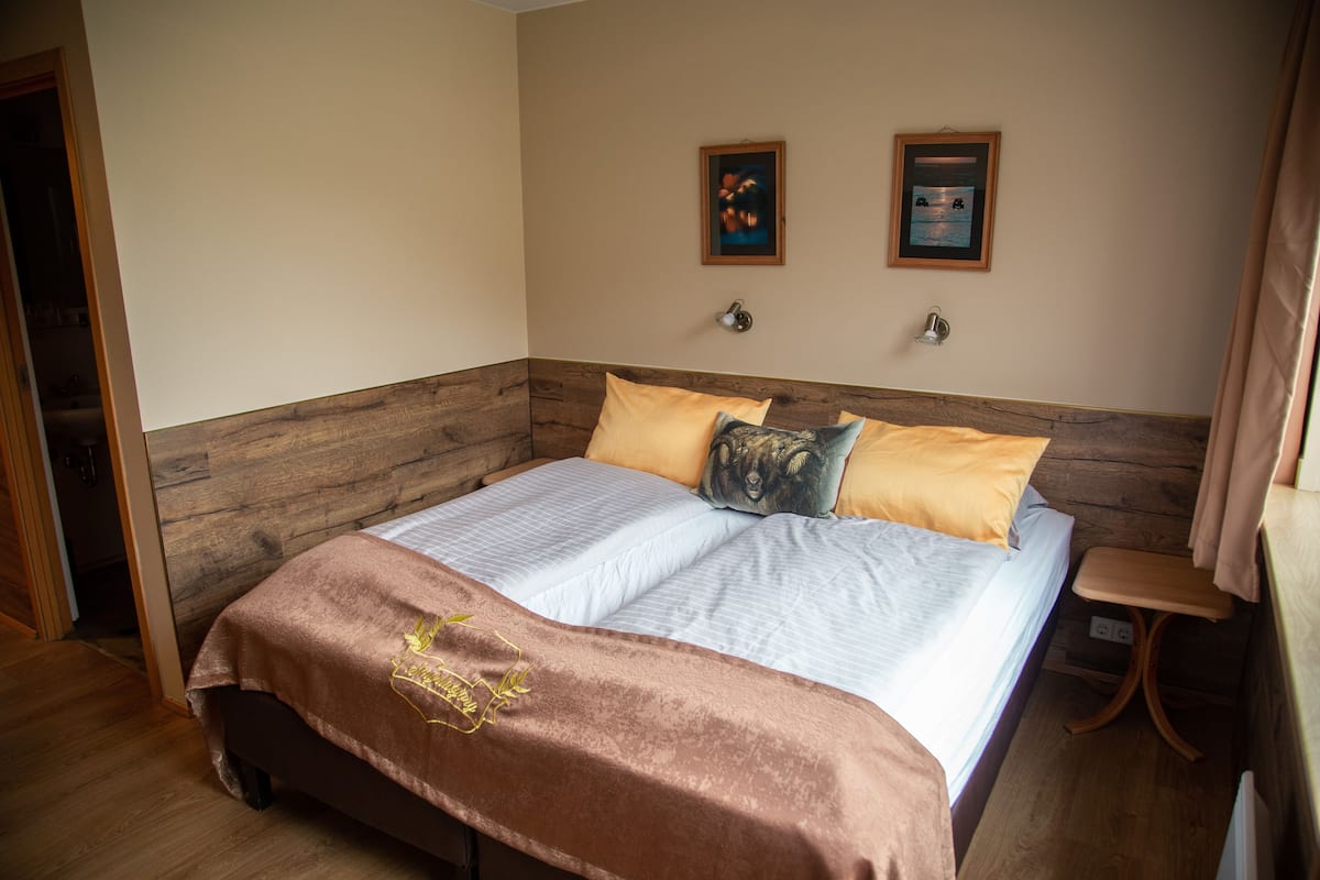 A bedroom with a wooden headboard, a bed with a brown blanket, two pillows, and two wall-mounted lamps.