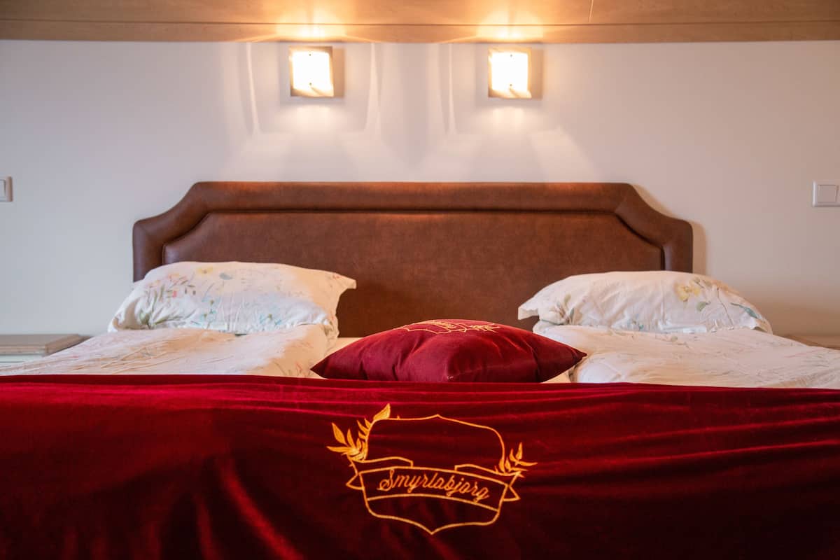 A bed with a red blanket and a pillow, two wall-mounted lights, and a wooden headboard.