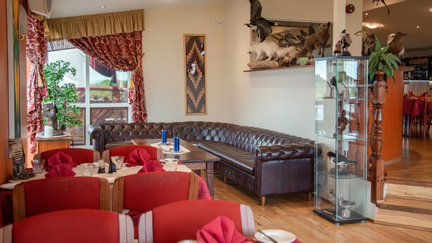 A dining area with a leather sofa, red chairs, and a glass display case with bird figurines. - Hotel Smyrlabjorg (Höfn)