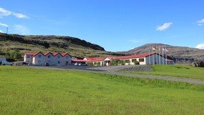 A building with multiple red-roofed units, a gravel driveway, and flags on the right. - Hotel Smyrlabjorg (Höfn)