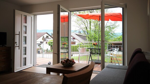 Ein Zimmer mit Holztisch, Obstschale und Blick auf einen Garten mit Sonnenschirm.