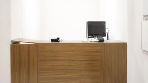 A wooden reception desk with a flat-screen monitor, a telephone, and a small white box. - Itsy Hotels Kamron (Mohali)
