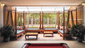 A pool area with wooden benches and a red pool table, surrounded by potted plants and a wooden fence. - Nonnee (Karon)