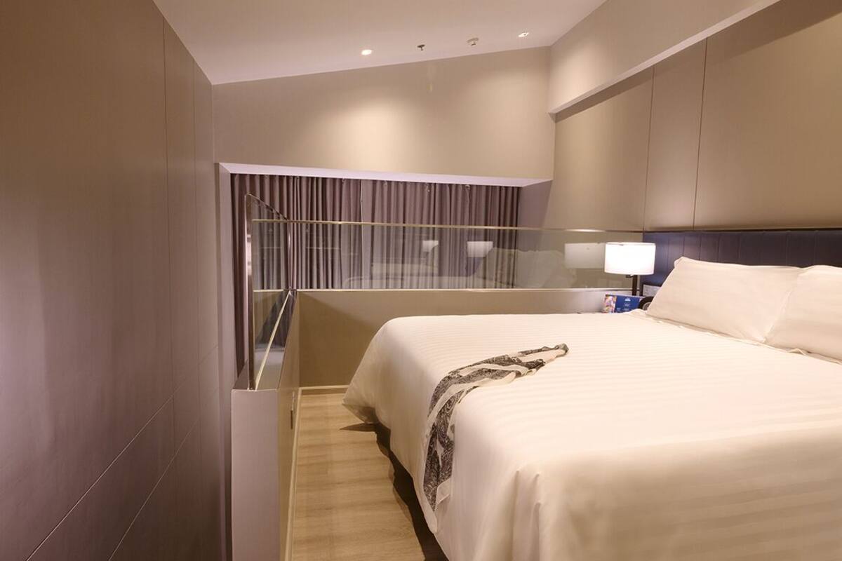 Ein modernes Hotelzimmer mit einem großen Bett, einer Glastrennwand und einem Nachttisch mit Lampe.