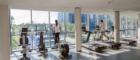 A gym with cardio machines, a rowing machine, and a large window offering a view of a bridge and greenery.