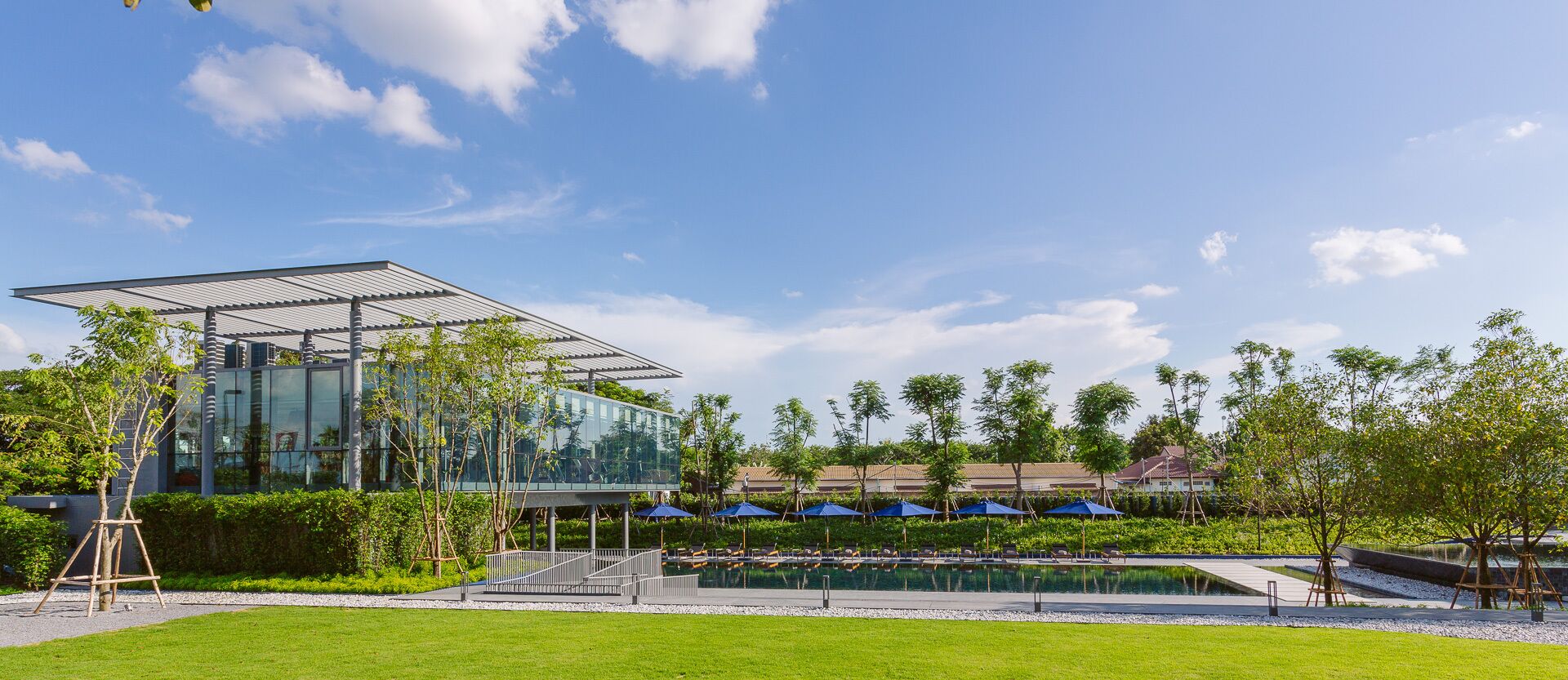 A modern building with a glass facade, a swimming pool, and outdoor seating areas.