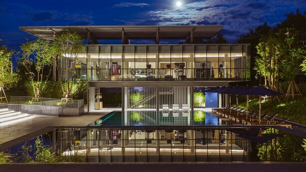 Un edificio moderno de dos pisos con fachada de vidrio, piscina y asientos al aire libre.