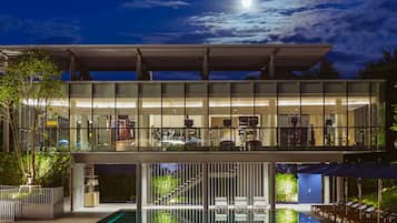 A modern two-story house with a glass facade, a pool, and a covered outdoor seating area.