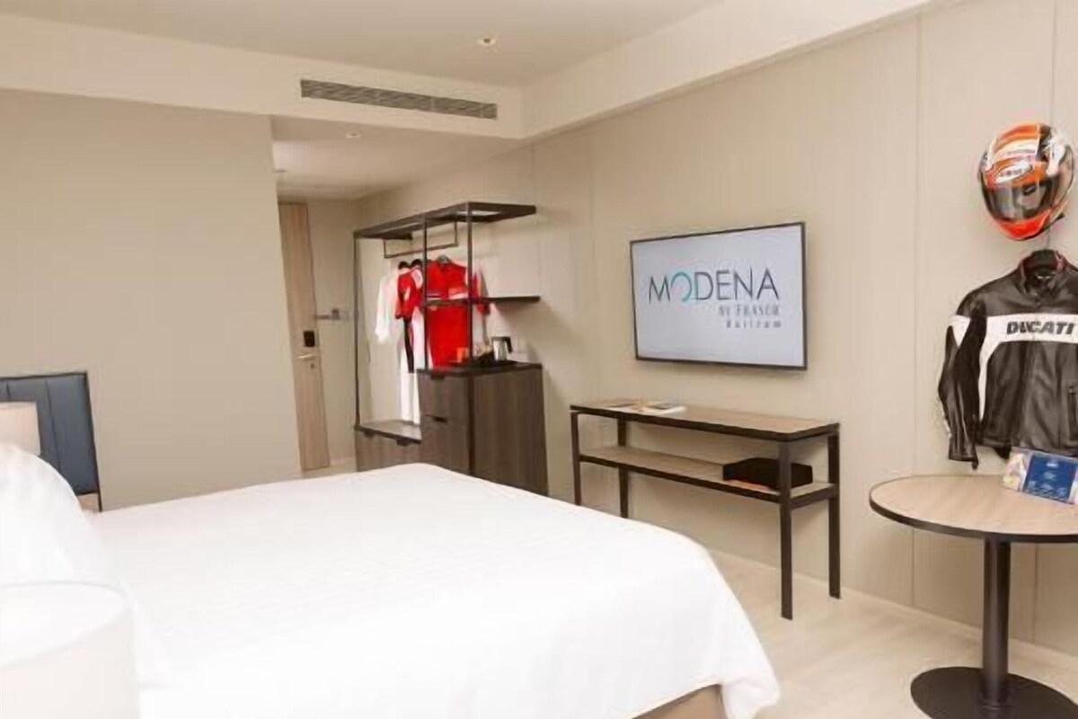 A hotel room with a bed, a desk, a wardrobe, and a wall-mounted TV.