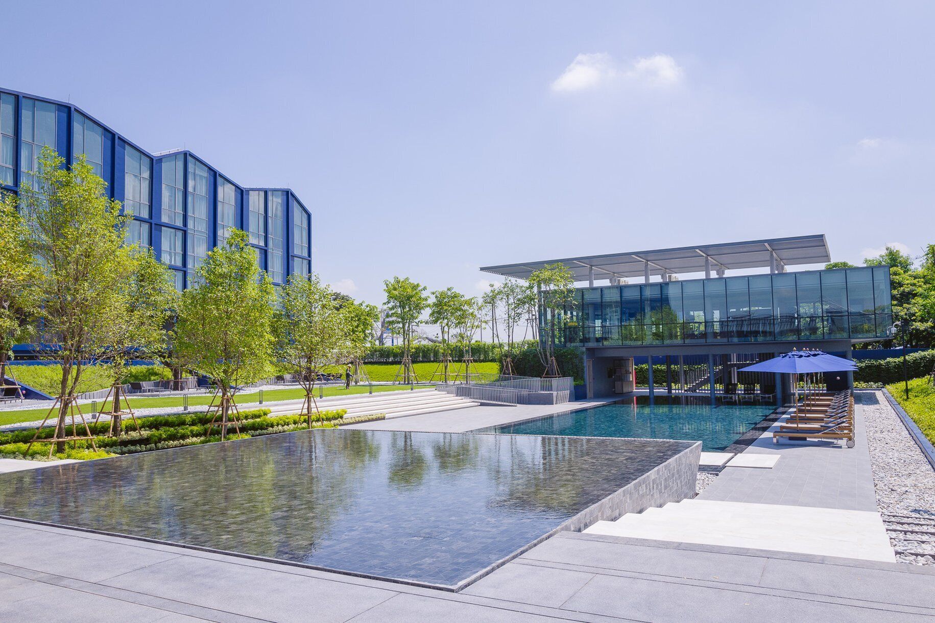 Un edificio moderno con fachada de vidrio, piscina y zonas de estar al aire libre.