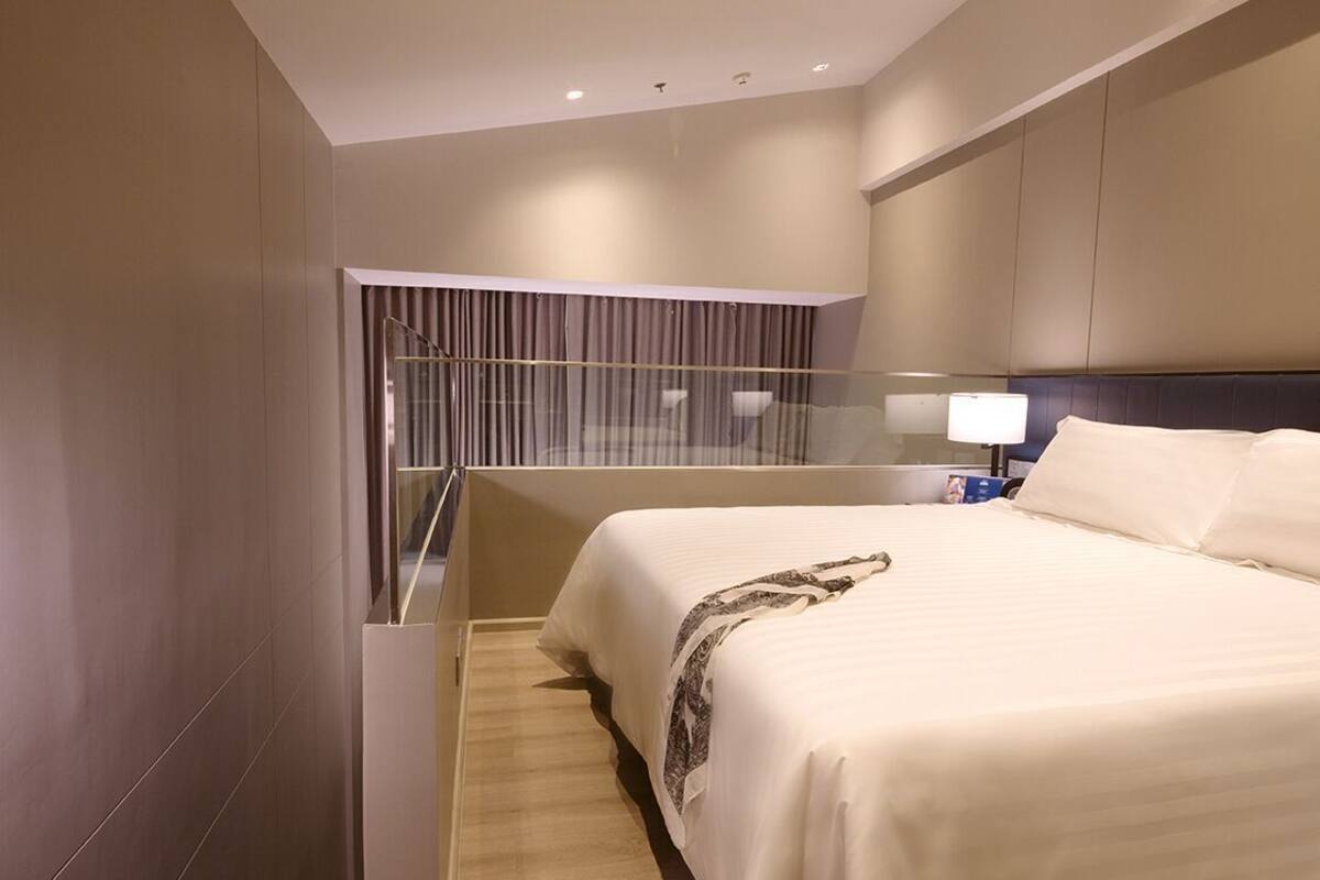 Ein Hotelzimmer mit einem großen Bett, einer Glastrennwand, einem Nachttisch und einer an der Wand befestigten Lampe.