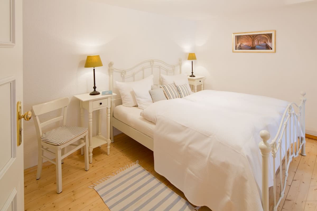 Une chambre à coucher avec un lit, deux tables de chevet avec des lampes, une chaise, un plancher en bois et un tableau au mur.
