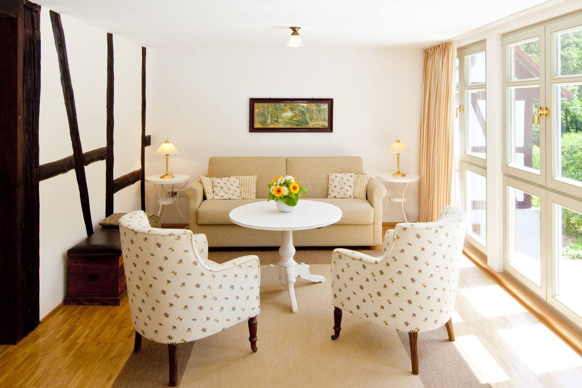 Une pièce comprenant un canapé, deux fauteuils, une petite table ronde avec un vase et un tableau accroché au mur.