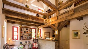 A spacious room with exposed wooden beams, a central island with a sink, and a cozy seating area with a red chair and bookshelves. - Romantik Hotel Landhaus Bärenmühle (Frankenau)