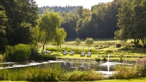 A serene garden with a pond, lush greenery, and several lounge chairs. - Romantik Hotel Landhaus Bärenmühle (Frankenau)