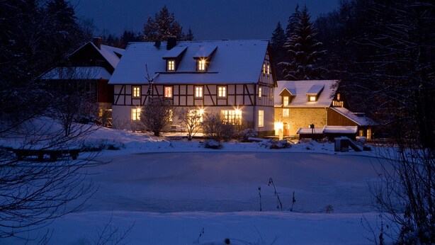 A large, traditional chalet with multiple windows and a snow-covered roof, surrounded by trees. - Romantik Hotel Landhaus Bärenmühle (Frankenau)