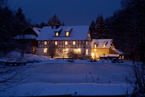 A large, traditional chalet with multiple windows and a snow-covered roof, surrounded by trees. - Romantik Hotel Landhaus Bärenmühle (Frankenau)