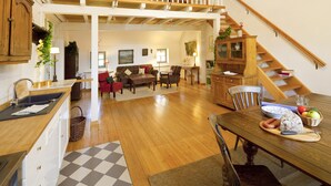 A spacious loft-style living area with a wooden staircase, a dining table set with food, and a cozy seating area. - Romantik Hotel Landhaus Bärenmühle (Frankenau)
