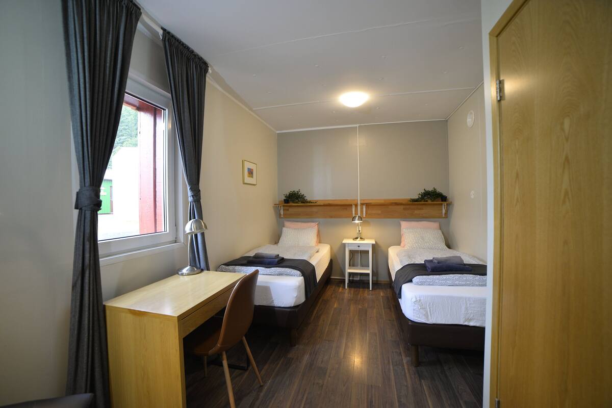 A compact room with two single beds, a desk, and a chair.