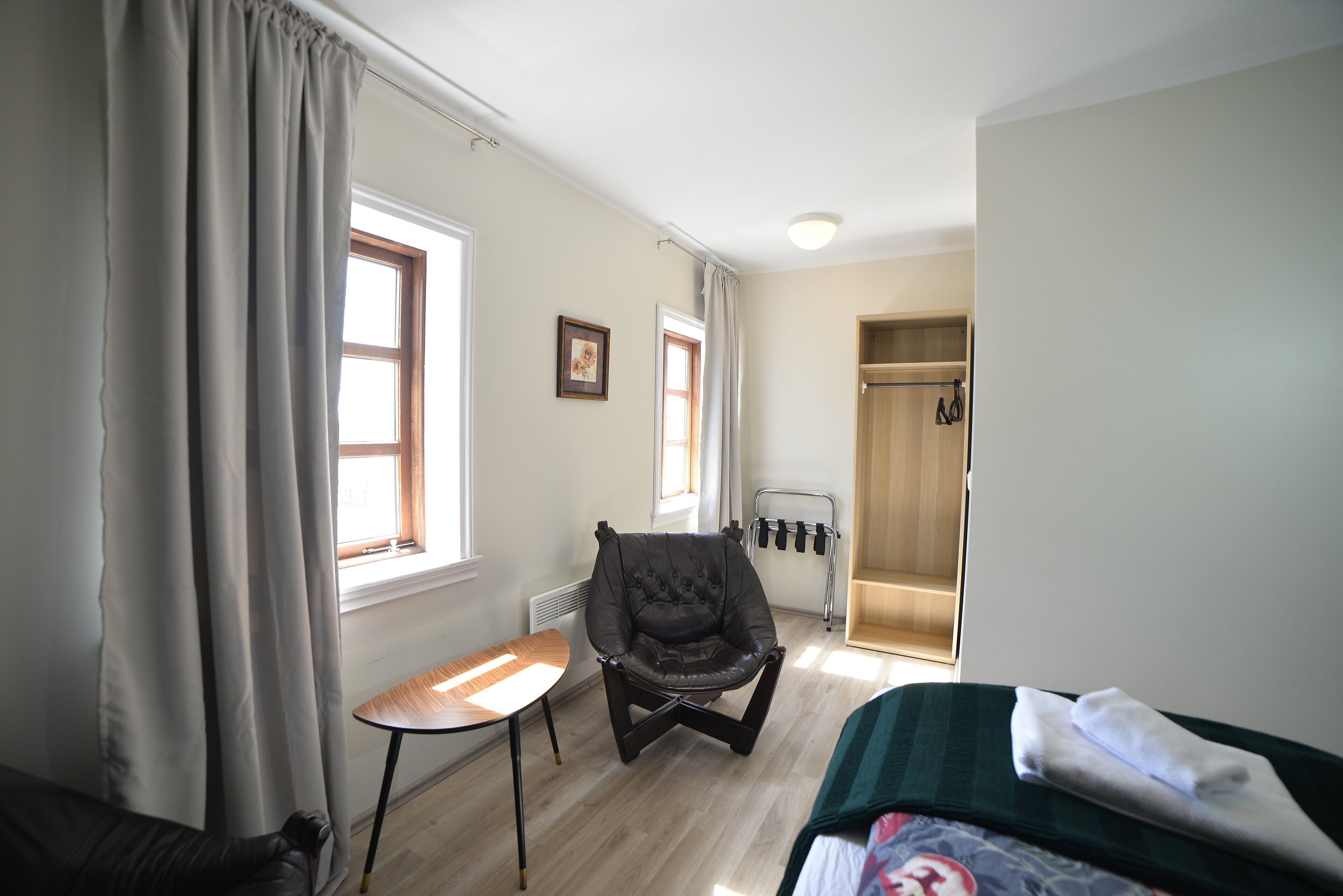 A room with a bed, a chair, a small table, and a window with curtains.