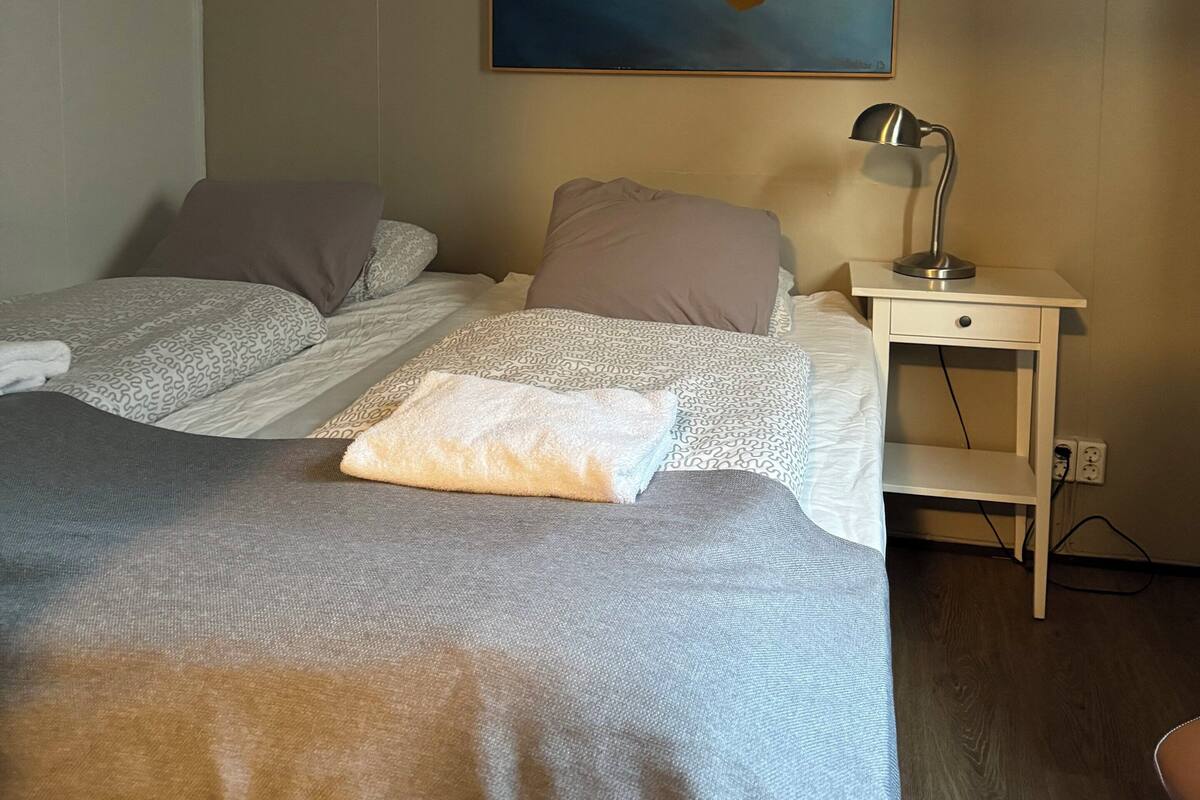 A bedroom with a bed, pillows, a bedside table with a lamp, and a painting on the wall.