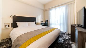A hotel room with a large bed, a desk, a television, and a window with curtains.