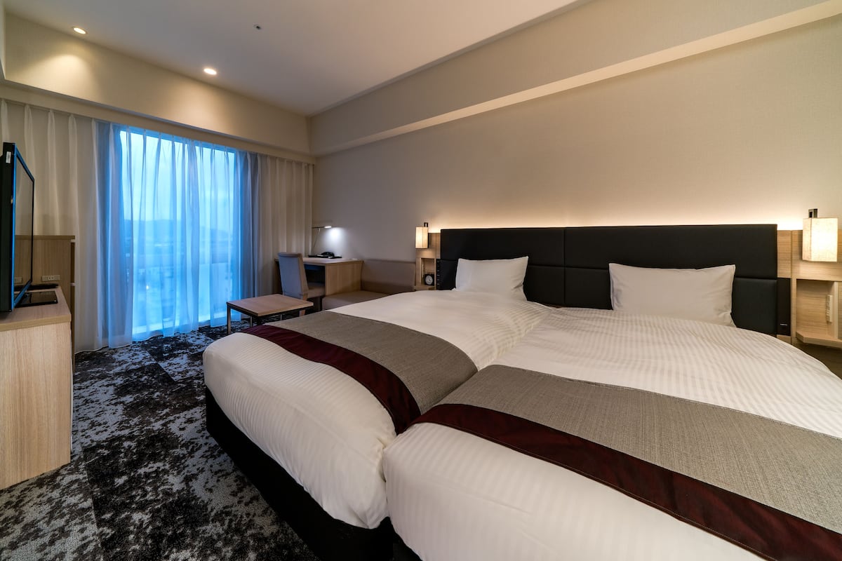 Ein Hotelzimmer mit einem großen Bett, einem Schreibtisch, einem Sessel und einem Fenster mit Vorhängen.