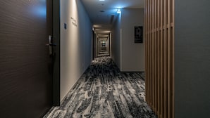 Un couloir d'hôtel avec un sol recouvert de moquette, un lambris en bois sur le côté droit et un panneau indiquant les numéros de chambre sur le côté gauche.