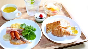 A tray with breakfast items including eggs, sausages, croissants, and a glass of orange juice.