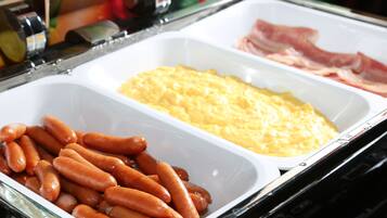 A buffet table with trays of sausages, scrambled eggs, and ham.