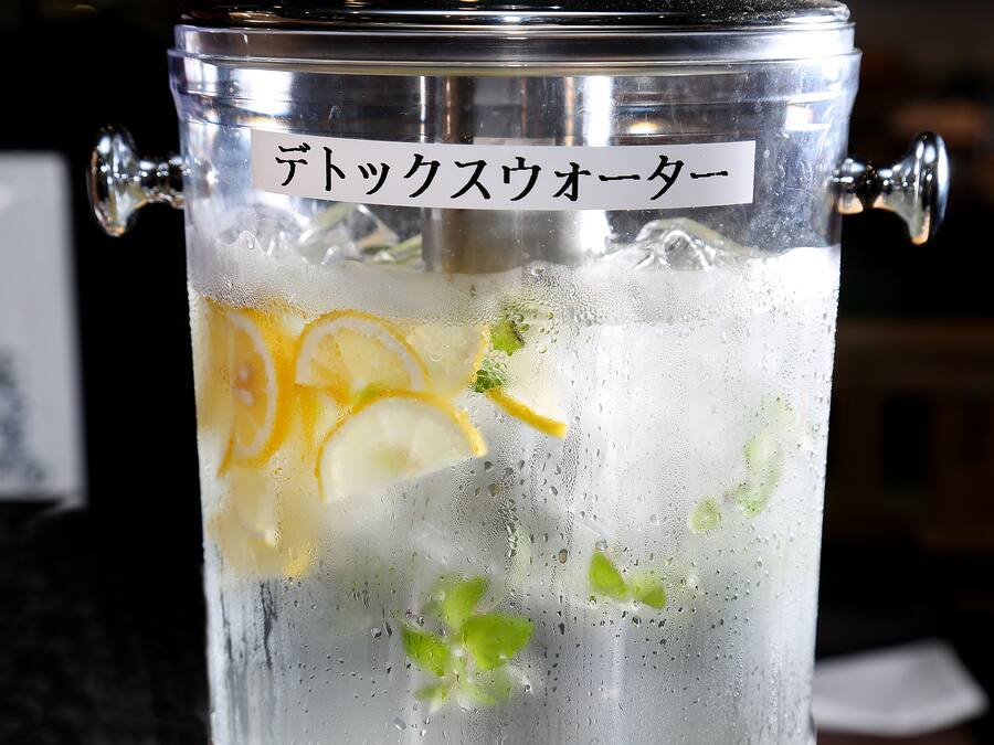A clear glass container with a metal tap, containing a beverage with lemon slices and mint leaves.