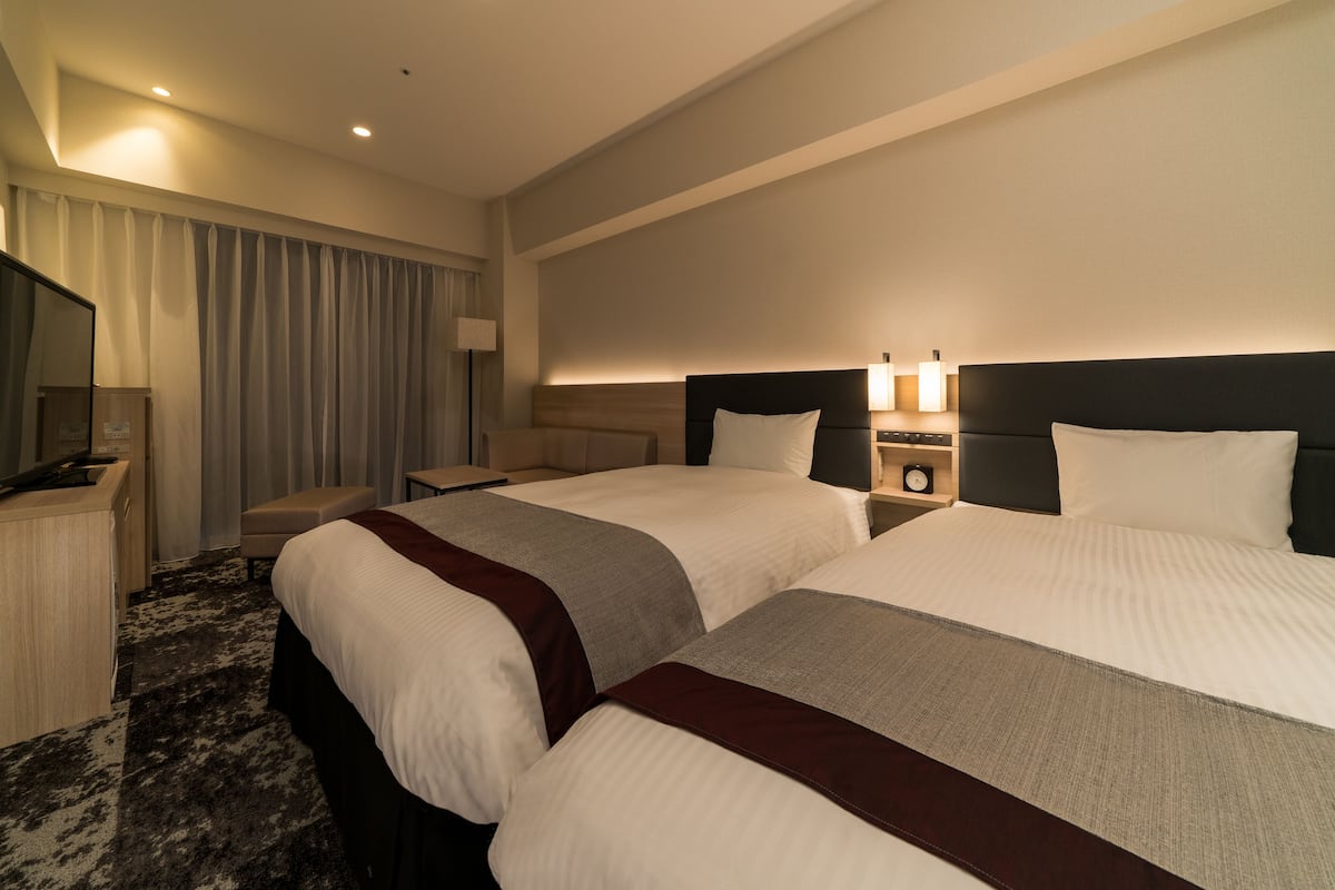 Ein Hotelzimmer mit zwei Betten, einem Schreibtisch, einem Stuhl, einem Fernseher und einer Lampe.