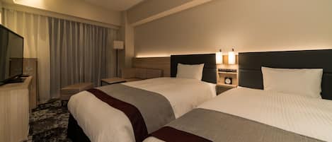 A hotel room with two beds, a desk, a chair, a TV, and a lamp.