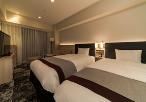 Habitación de hotel con dos camas, un escritorio, una silla, un televisor y una lámpara.