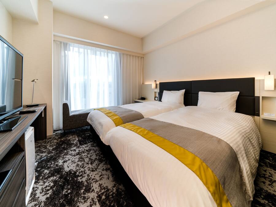 Een hotelkamer met twee bedden, een televisie, een bureau en een groot raam met gordijnen.