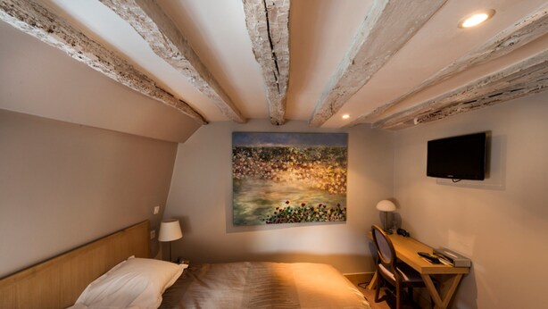 Un dormitorio con cama, escritorio, silla, un cuadro y televisor en la pared.