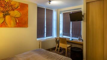 Ein Hotelzimmer mit Bett, Schreibtisch mit Stuhl, Wandfernseher und einem Vorhangfenster.