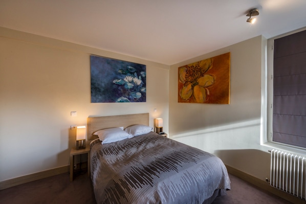 Un dormitorio con una cama, dos mesitas de noche y dos lámparas de pared.
