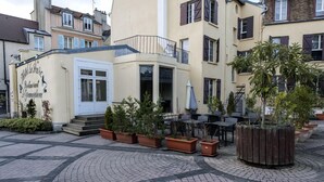 Un restaurante con terraza al aire libre, rodeado de macetas con plantas y un patio empedrado.