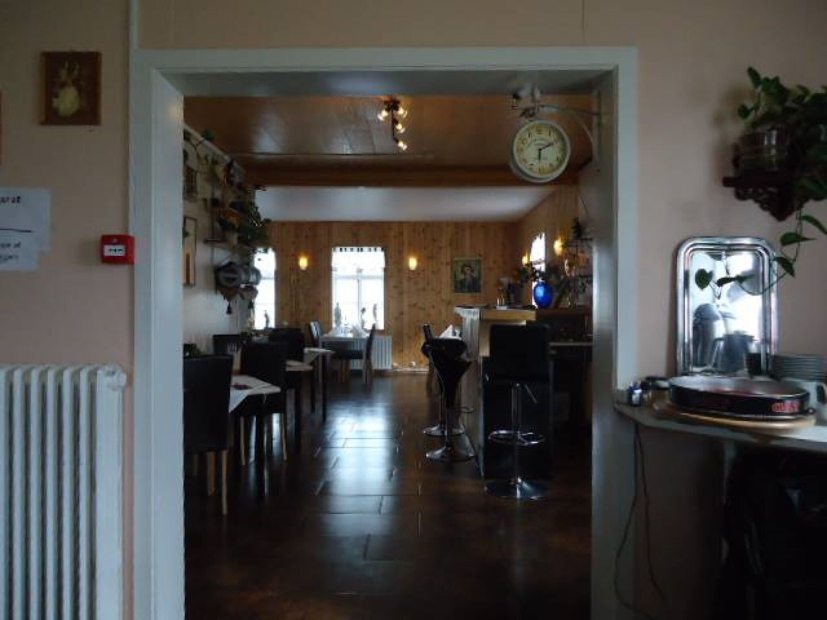 A restaurant with a wooden interior, a clock on the wall, and a bar area with a mirror and plant.
