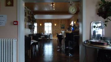 A restaurant with a wooden interior, a clock on the wall, and a bar area with a mirror and plant.