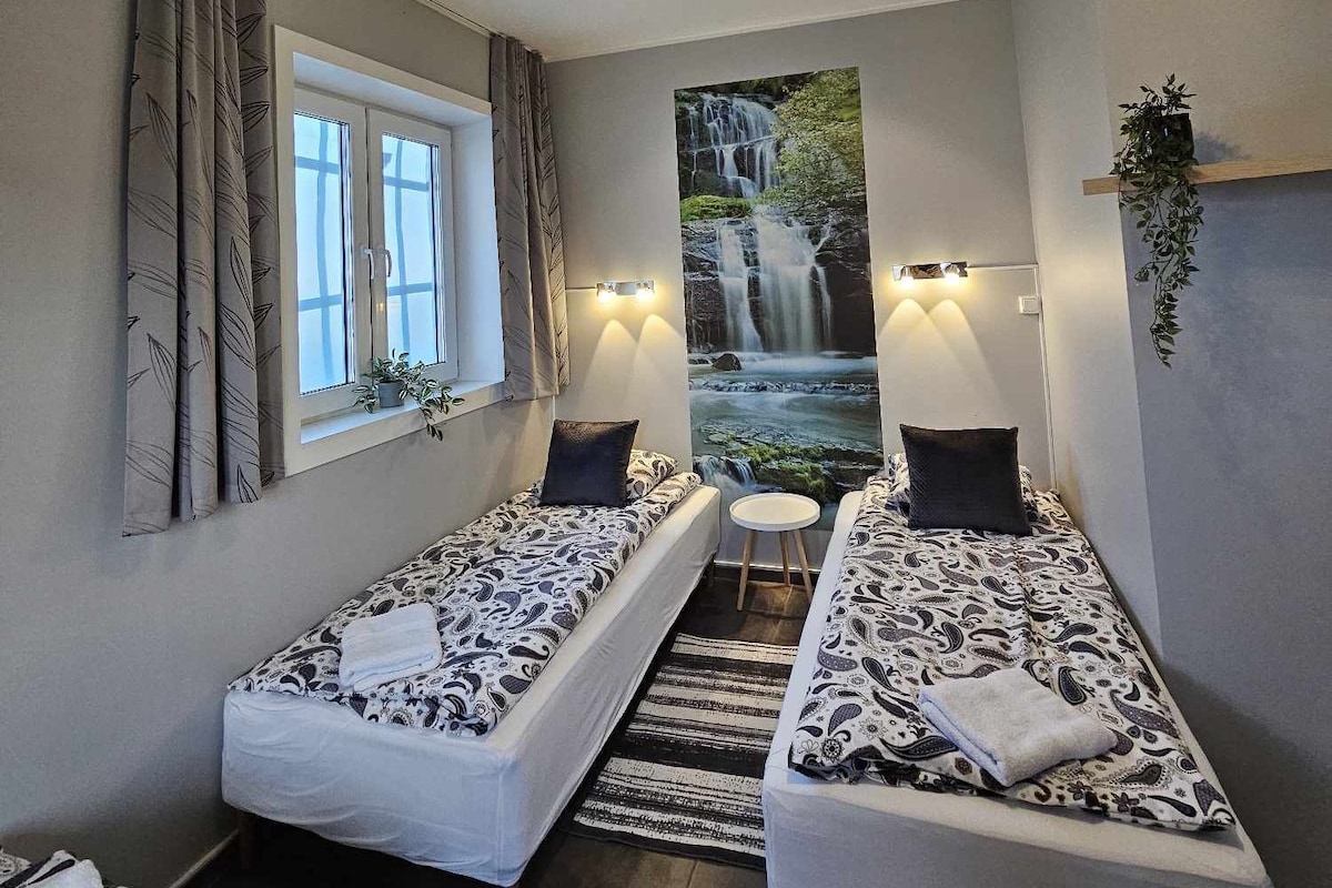 A small, cozy room with two single beds, a window, a wall-mounted TV, and a small table.
