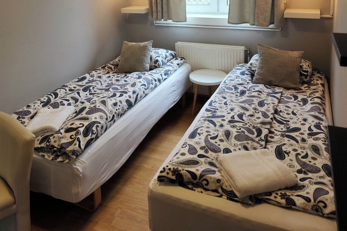 A small, cozy room with two single beds, a small table, and a chair.