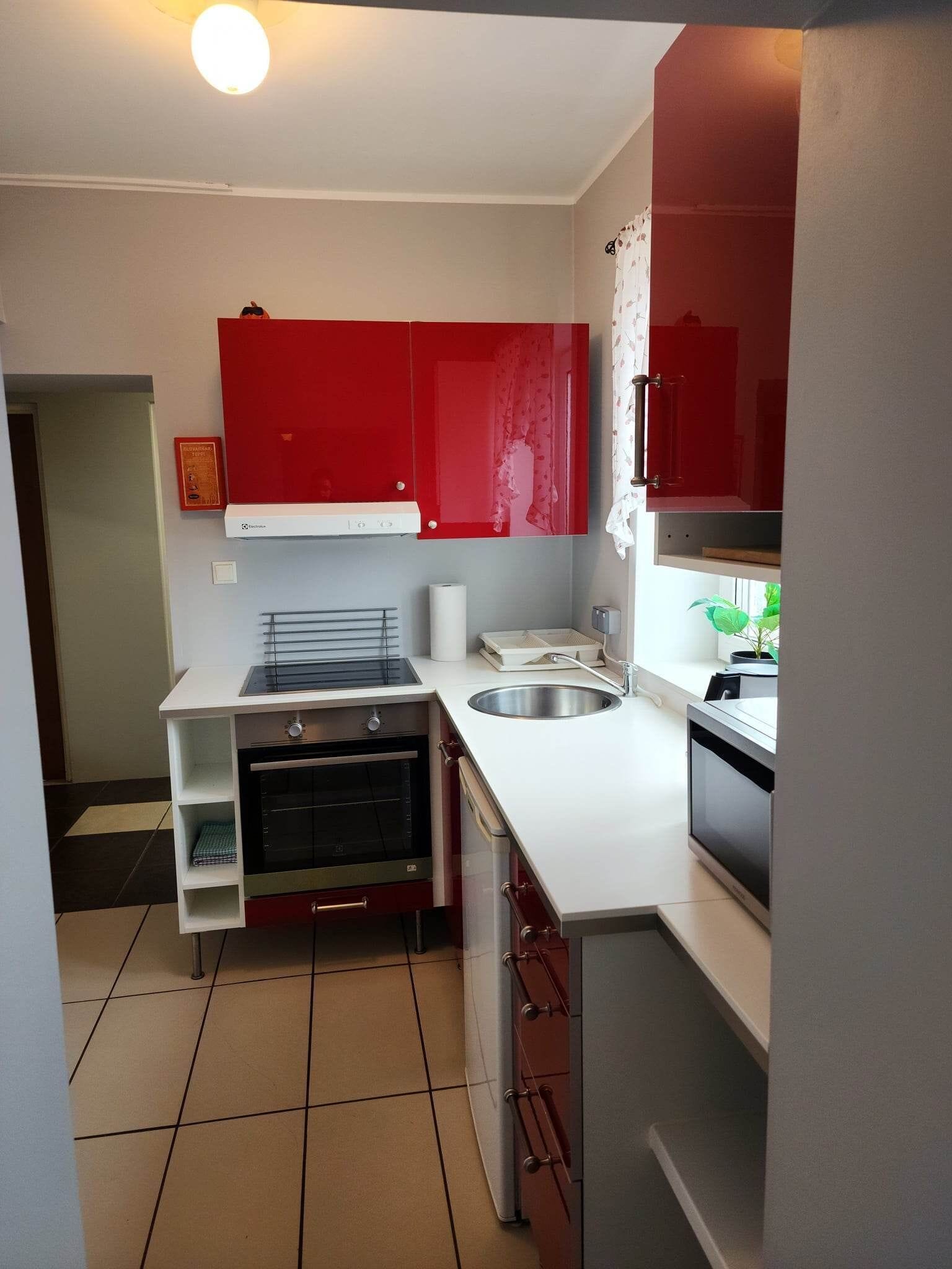 A compact kitchen with red cabinets, a built-in oven, a microwave, and a sink.