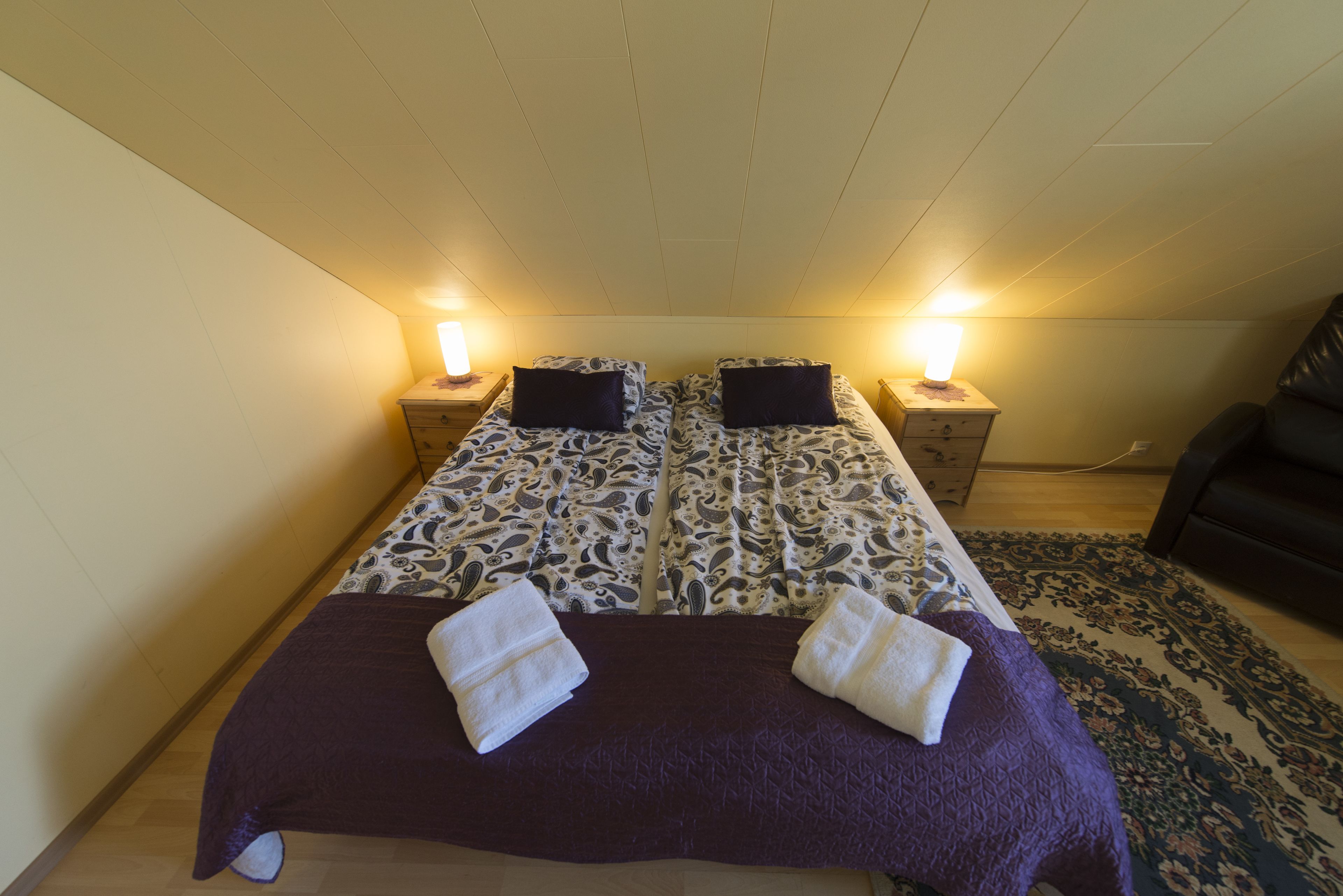 Una cama con dosel y ropa de cama estampada, dos lámparas de noche y un sofá de color oscuro en una habitación con piso de madera y alfombra estampada.