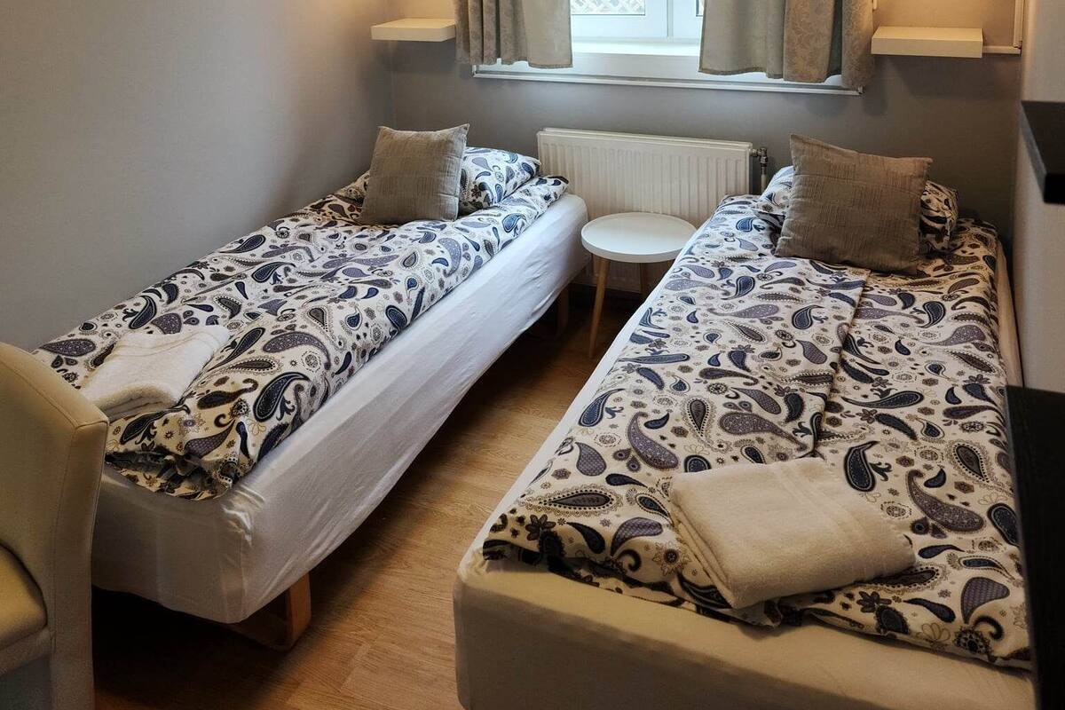 A small, cozy room with two single beds, a small table, and a chair.